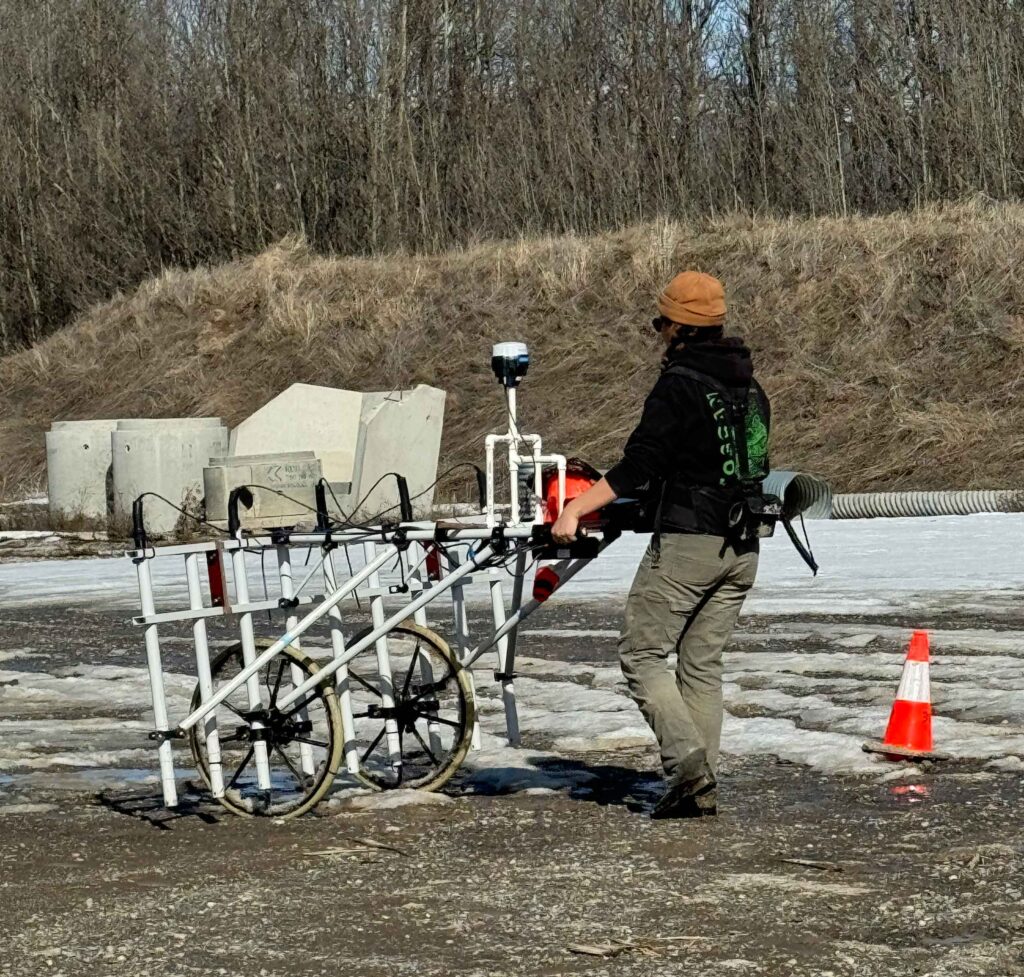 Person maneuvering ground-penetrating scanner over land